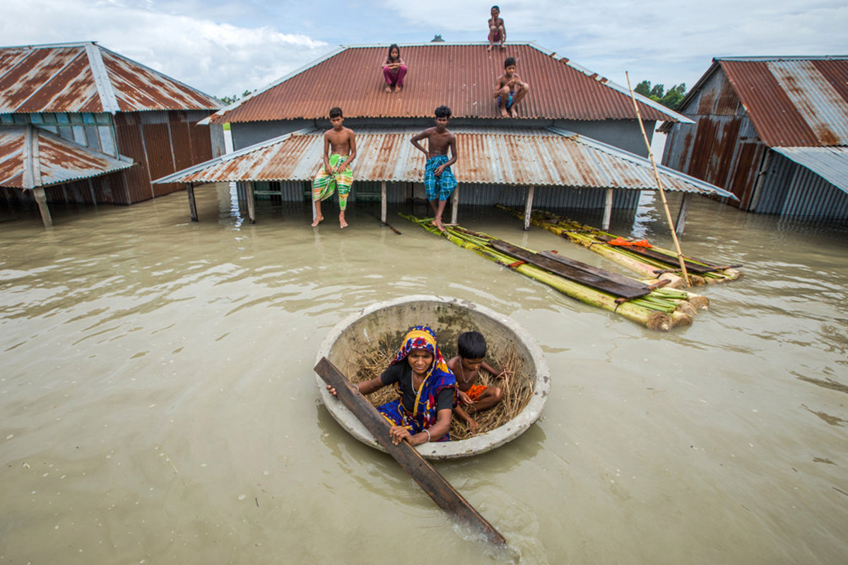 Lampoon floods affect people, a house almost submerged, family members on the roof and in a small, coracle Moniruzzaman Sazal, Climate Visuals Countdown