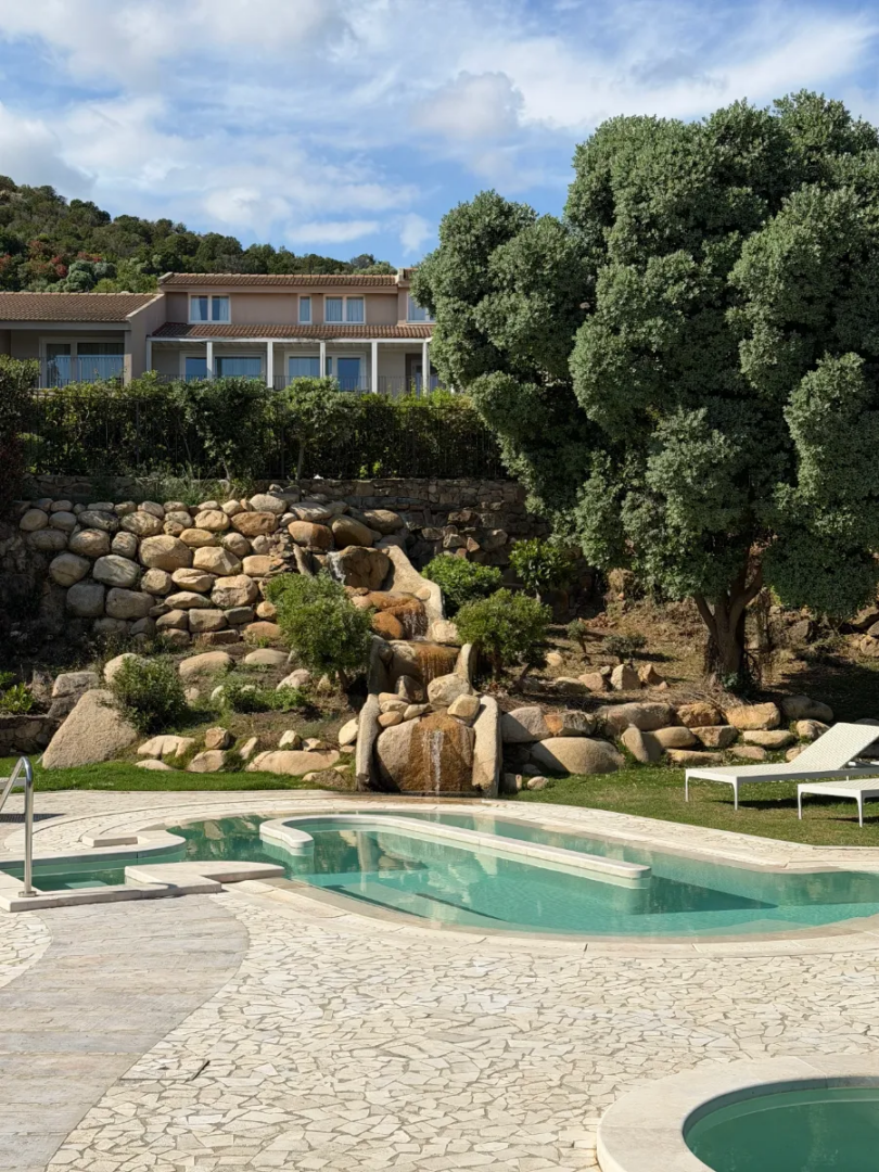 Area piscine del Chia Laguna Nature Resort, inserita tra rocce granitiche, vegetazione mediterranea e percorsi d’acqua integrati nel paesaggio