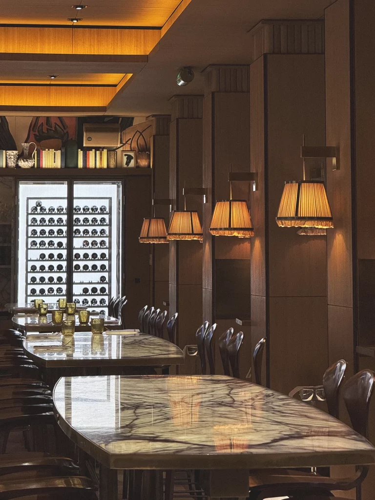 Brach Paris, Mediterranean dining room – Pleated pendant lamps cast warm pools of light over olive-wood tables, completing Chef Adam Bentalha’s sunny mise-en-scène.