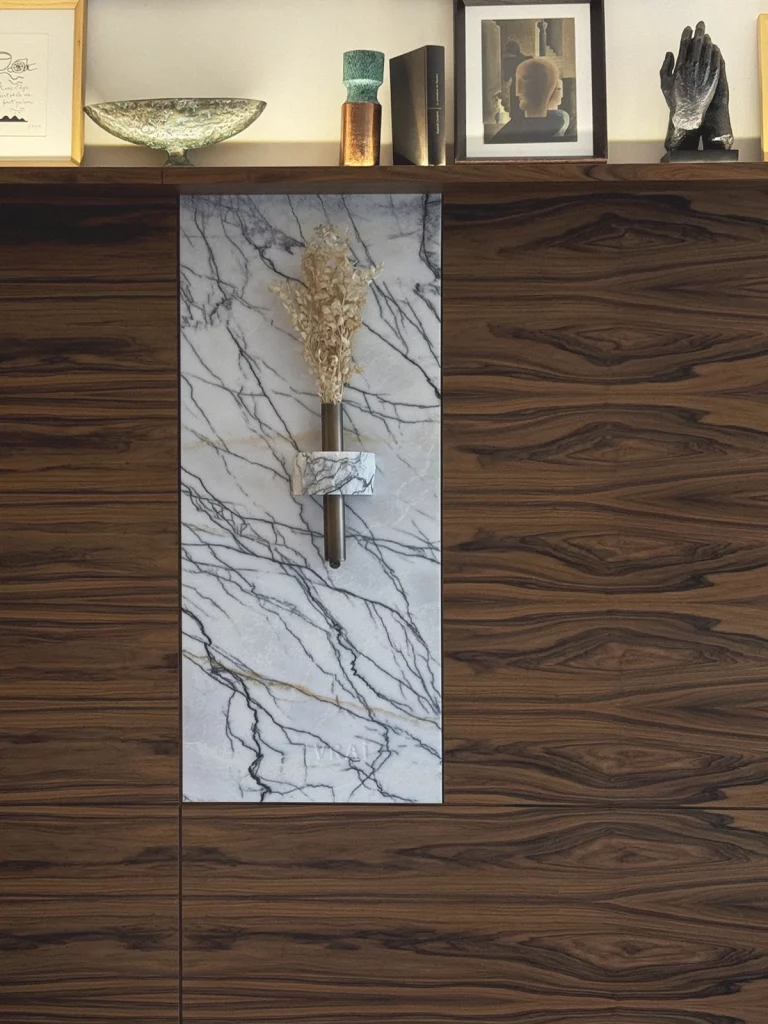 Brach Paris, suite detail – A vein-cut Carrara marble niche cradles a single dried bloom, nesting minimalist calm inside book-lined rosewood shelving