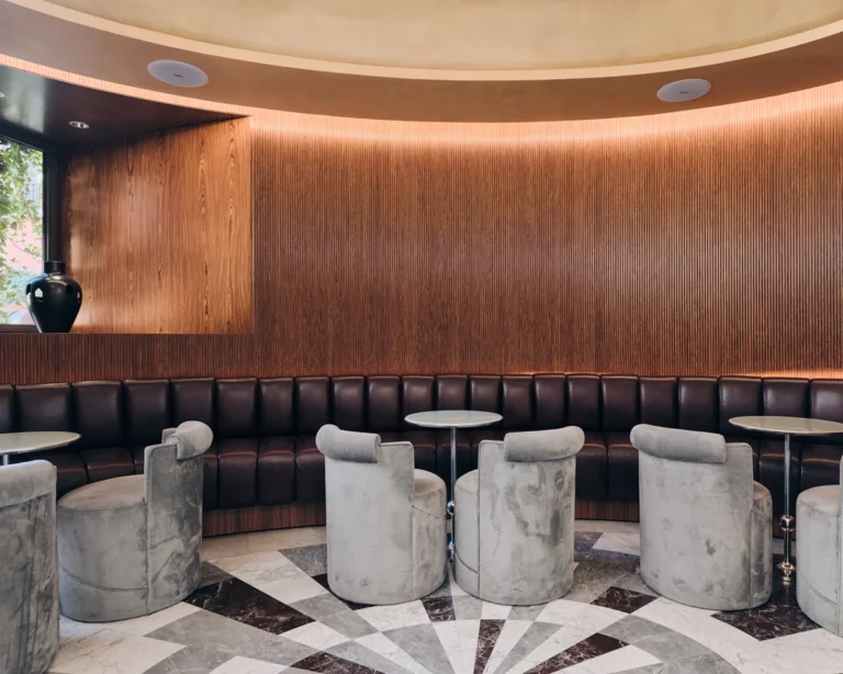 sculptural sofa that blends comfort and contemporary design in W Rome’s lounge|Marble steps and a golden dome set the stage for stylish gatherings at W Rome|Contrasting textures of travertine and rich wood create a refined statement at W Rome|Art and reflections combine at the W Rome. Ph. Luca Santini|A modern rattan sconce adds a warm