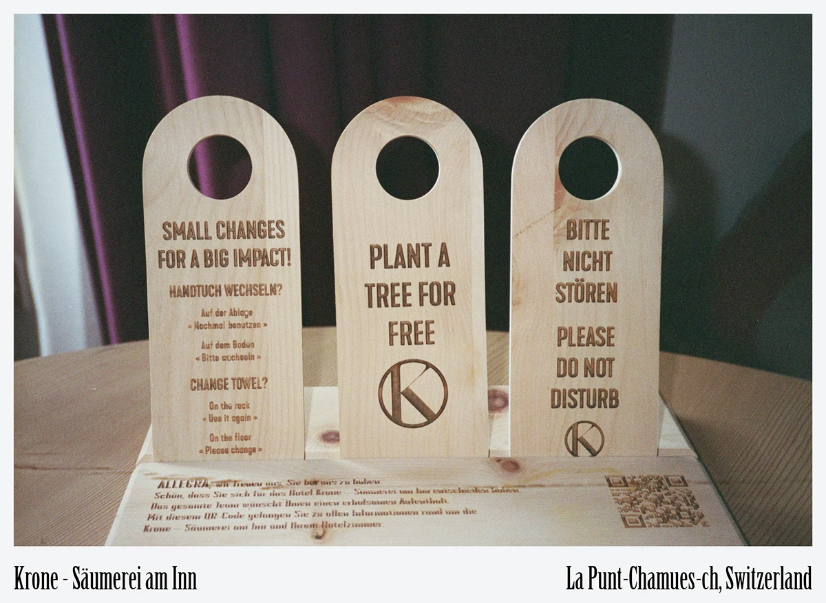 Krone La Punt Engadin sustainable hotel interior|Upcycled wooden door hangers promoting tree planting at Krone La Punt hotel|Minimal pine-wood bedroom with locally woven linen fabrics at Krone La Punt Engadin|Patrician house turned eco-boutique hotel in La Punt Chamues-ch Engadin at Krone La Punt|Cozy reading niche beneath arched historic window at Krone La Punt Engadin|Deep-set window framing Alpine village view in sustainable stay at Krone La Punt|Close-up of reclaimed saddle-leather seating in sustainable design at Krone La Punt|Original 1500s restaurant doorway restored with local timber at Krone La Punt|Historic Engadin stone façade on the River Inn at Krone La Punt eco-hotel exterior|Reclaimed velvet lounge seating in low-impact design at Krone La Punt Hotel|Custom ash-wood shelving showcasing local ceramics and books at Krone La Punt|Breakfast table with panoramic valley view at Krone La Punt Engadin hotel|Naturally dyed hemp and wool textiles crafted nearby for Krone La Punt interiors