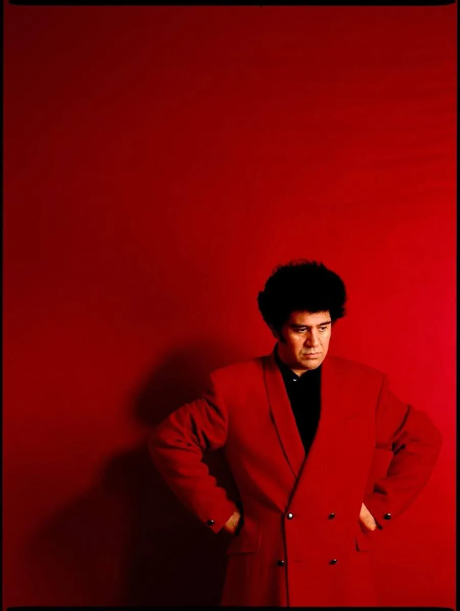 Pedro Almodóvar, photographed by Jorge Represa, stands against a vivid red background wearing a red suit.