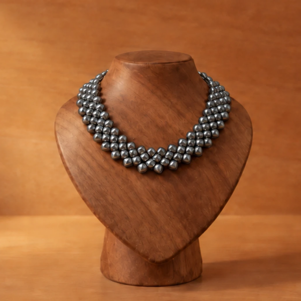 titanium necklace with rounded square elements, displayed on a sculpted wooden bust against a warm wood background