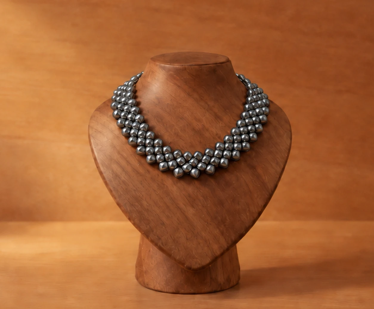 titanium necklace with rounded square elements, displayed on a sculpted wooden bust against a warm wood background
