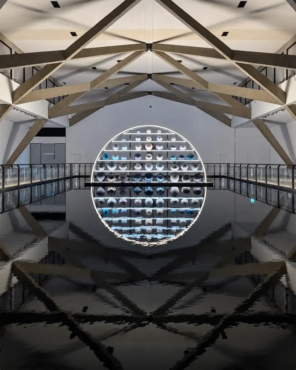 Circular illuminated installation of contemporary glass vessels reflected in a dark water surface inside the Homo Faber exhibition space in Venice
