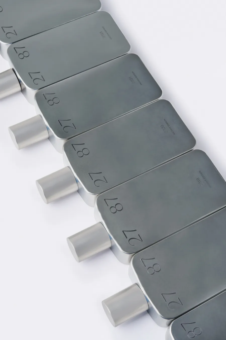 27 87 Archive Edition perfume bottles arranged diagonally, featuring brushed silver rectangular bodies, engraved numbers and cylindrical caps against a white background.