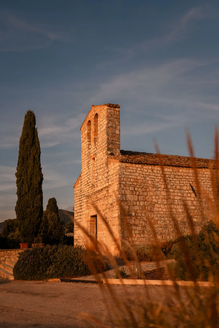 Medieval stone church of San Pietro a Pettine in Umbria, surrounded by cypress trees and vegetation in the evening sunlight.