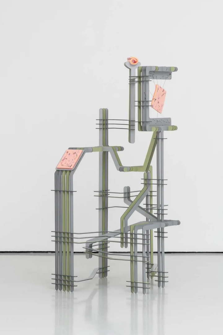 Abstract sculpture by Cem Örgen composed of interconnected gray and pale green structural forms, thin horizontal metal rods and pink panels against a white background.