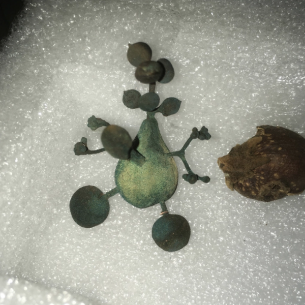 Green pewter Daphne sculpture with branching limbs and rounded forms resting on white foam beside a dried root.