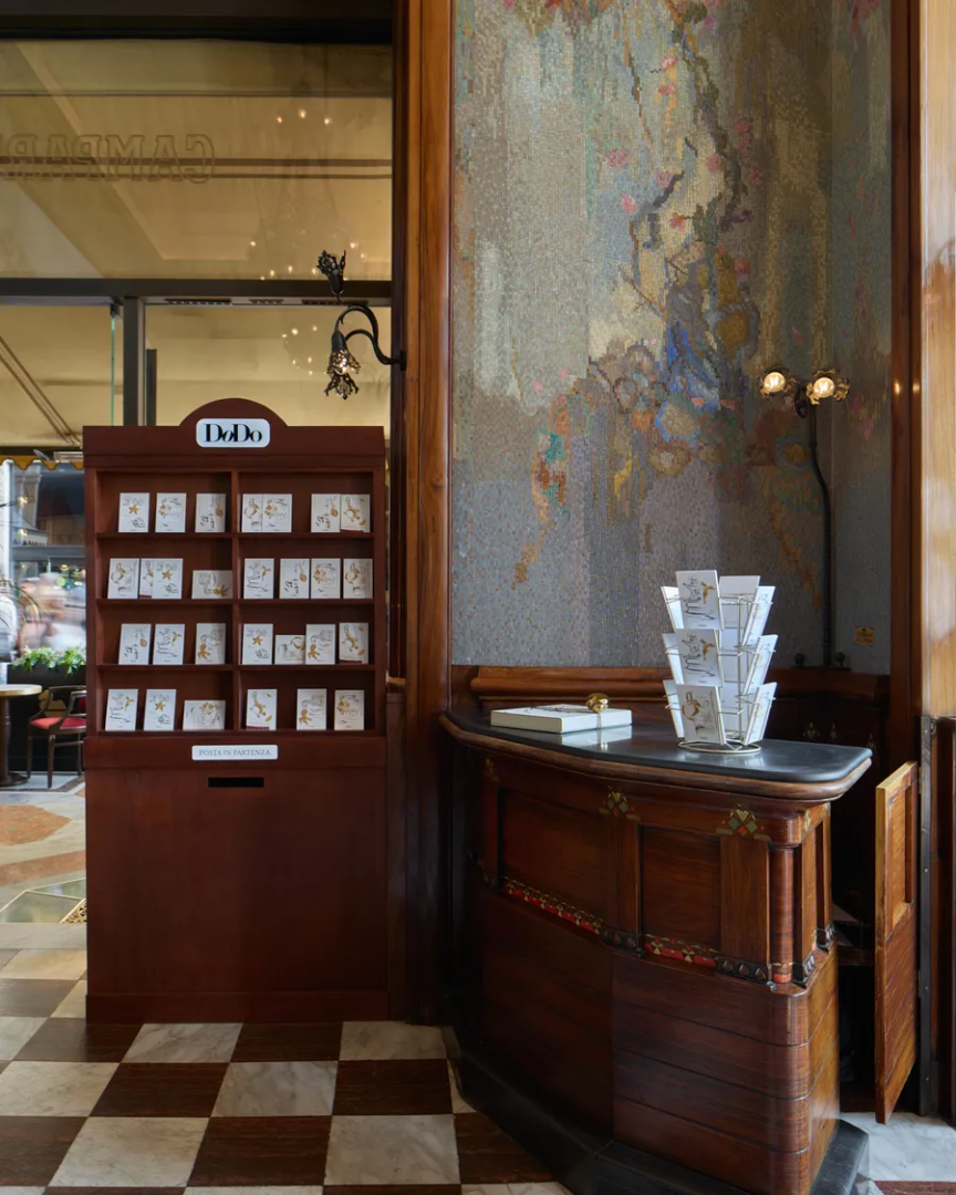 DoDo jewelry display inside Camparino in Galleria, featuring wooden counters, illustrated cards, decorative mosaic walls, and marble flooring.