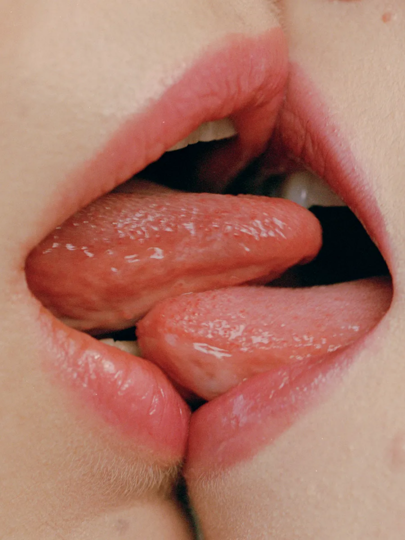 Macro photograph of two open mouths with overlapping tongues, showing the texture of lips, skin and saliva.