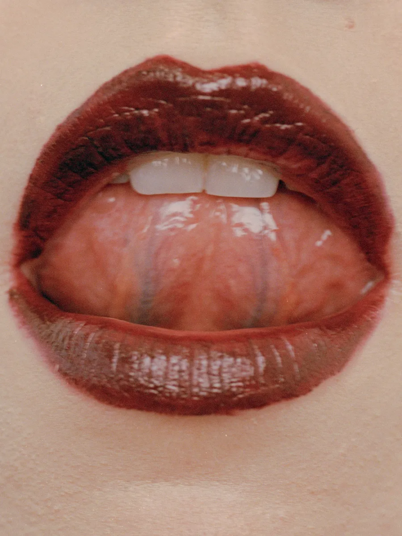 Extreme close-up of burgundy lips, exposed teeth and an extended tongue with visible moisture and skin texture.