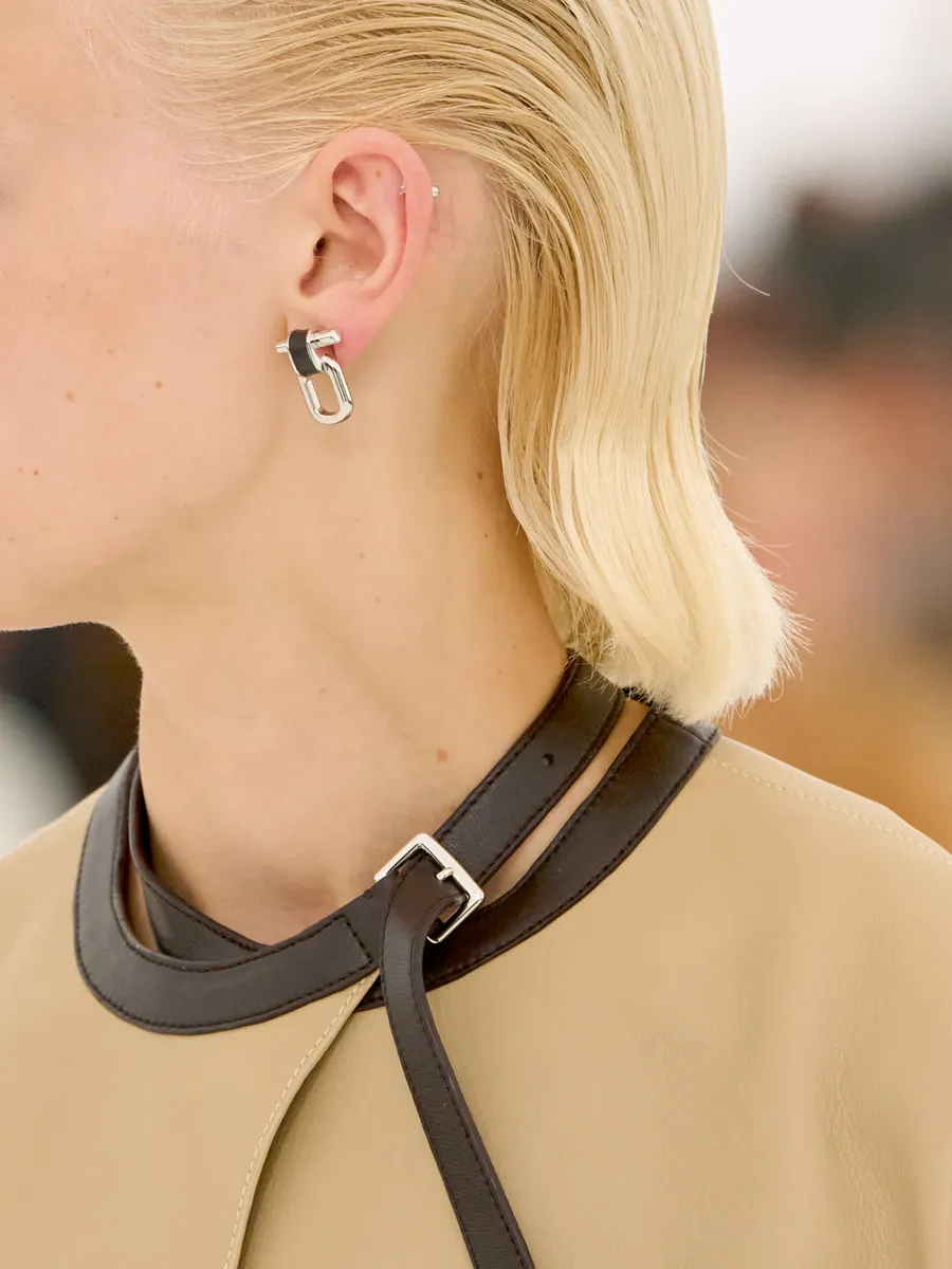Hermès SS27 leather neck strap with silver buckle and matching earring on a tan leather look.
