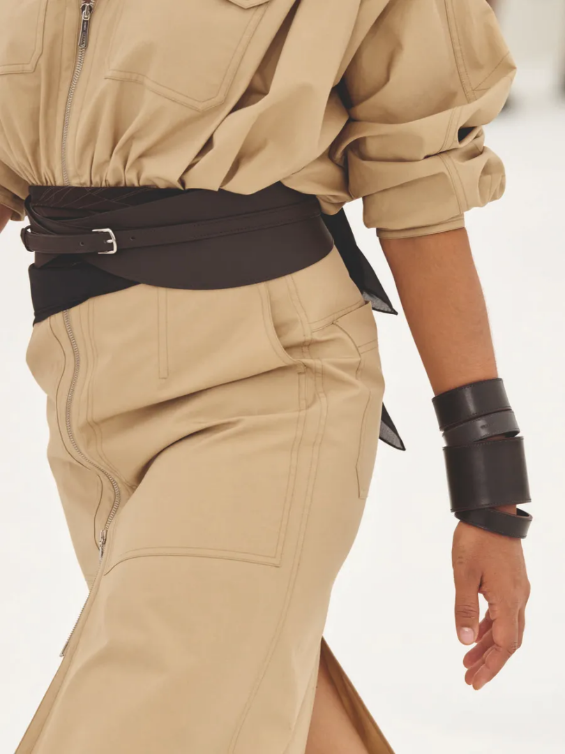 Hermès SS27 wide brown leather belt with buckle over a beige zippered look and stacked leather cuffs.