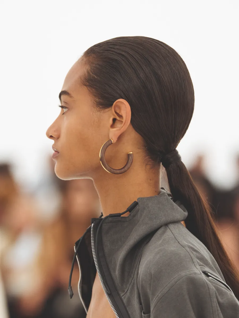 Hermès SS27 profile detail with large hoop earring and grey zippered garment