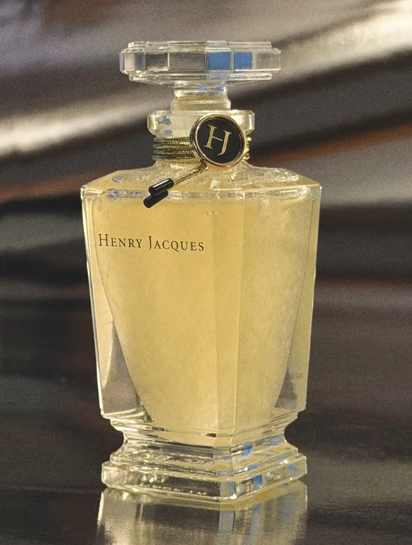Close-up of Henry Jacques Rose Snow de HJ perfume flacon, showing suspended particles in the pale yellow concentrate, crystal stopper and gold HJ medallion.