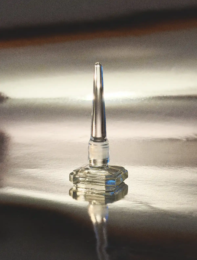Close-up of Henry Jacques Rose Snow crystal perfume bottle, showing the golden liquid, engraved lettering and glass facets.