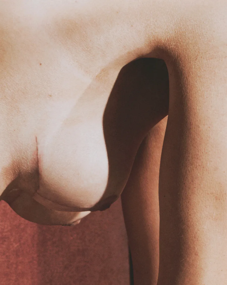 Artistic close-up of Maja Malou Lyse’s bare torso and arm, highlighting natural skin textures and dramatic shadows against a muted red background, photographed by Lalo + Eva