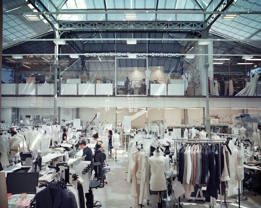 Interior of the Celine atelier in Paris, showing seamstresses at work, dress forms, garment racks and sewing stations beneath a glass and steel roof.