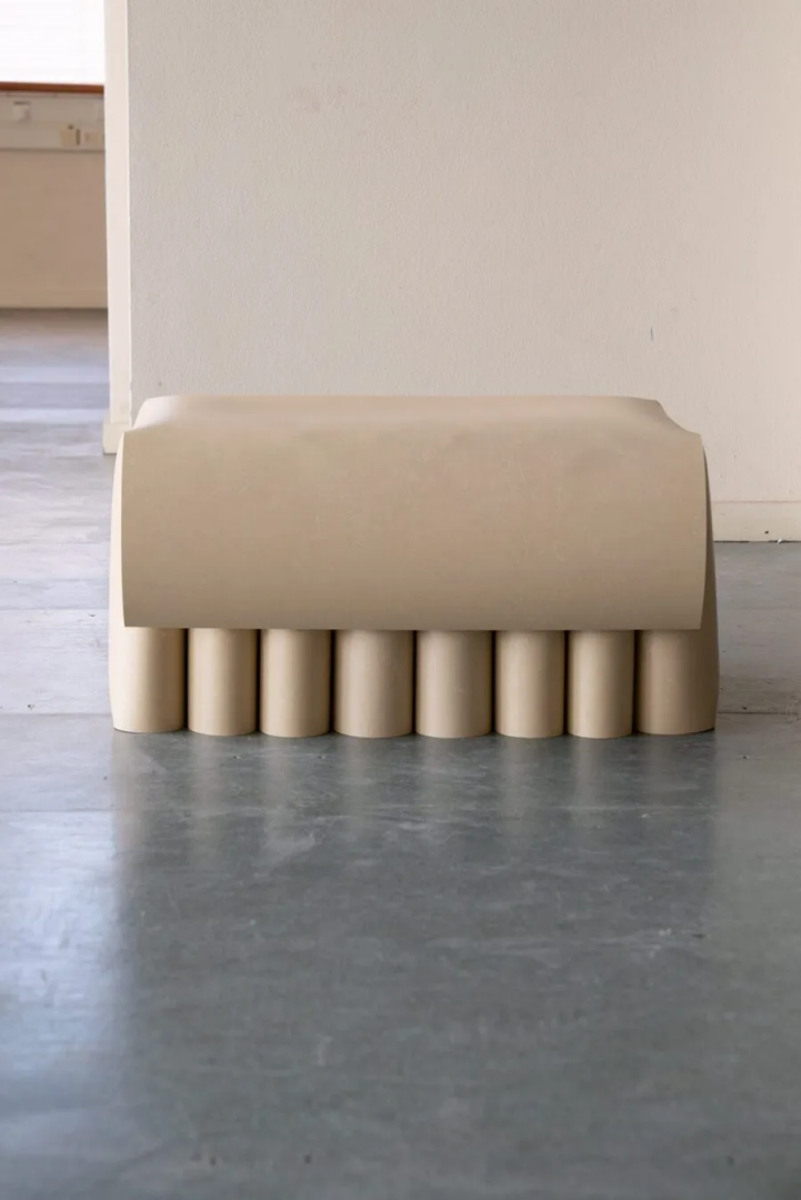Front view of a beige linoleum bench with a curved seat resting on eight cylindrical supports.