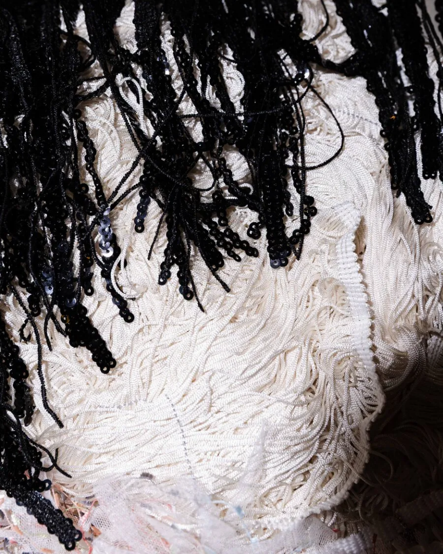 Close-up of black sequined fringe layered over white embroidered textile with loose threads and textured stitching, Lorenza Longhi at Centro Pecci.