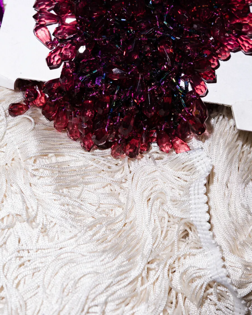Burgundy faceted beads and crystals layered over white fringed fabric, showing contrasting textile surfaces in Lorenza Longhi's work at Centro Pecci.