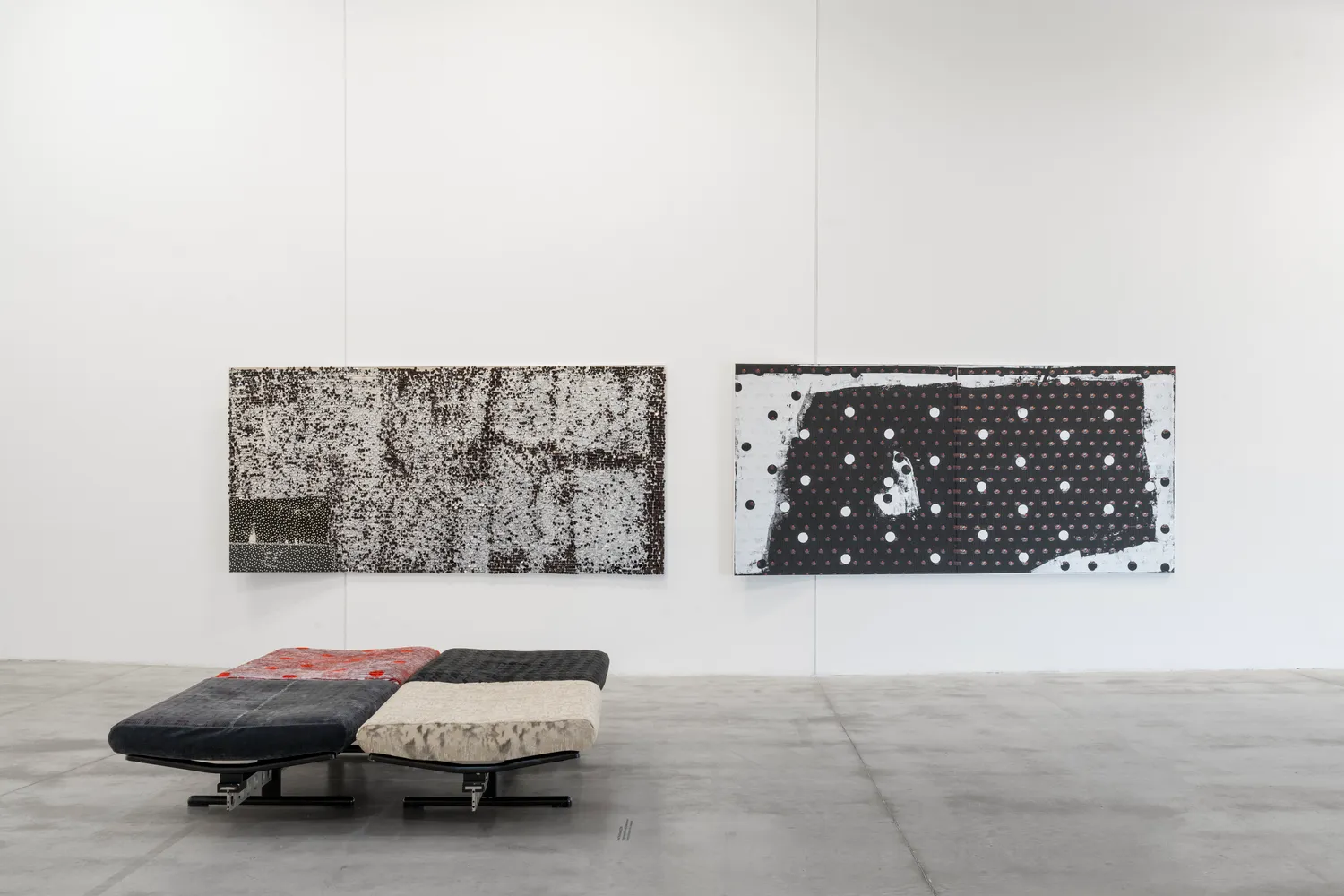 Installation view of Lorenza Longhi's exhibition at Centro Pecci, featuring two large black-and-white wall works and a low modular upholstered seating structure.