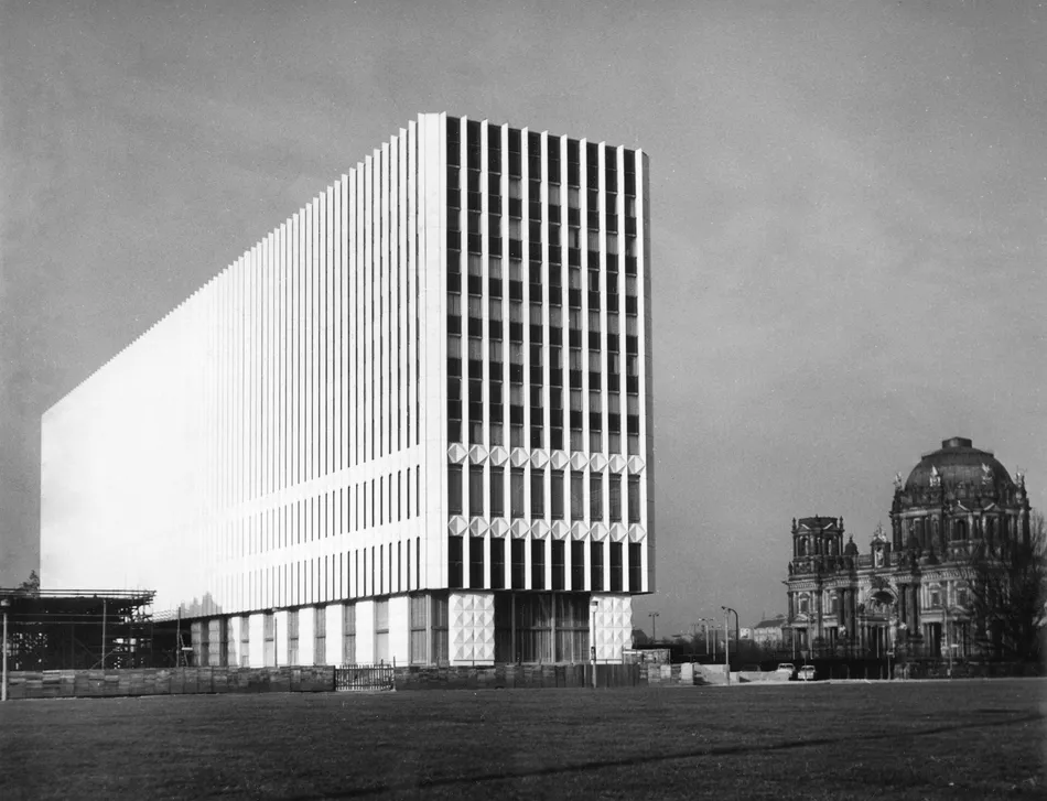 Black-and-white architectural photograph of the GDR Ministry of Foreign Affairs in Berlin, showing its geometric facade and the historic Berliner Dom in the background.