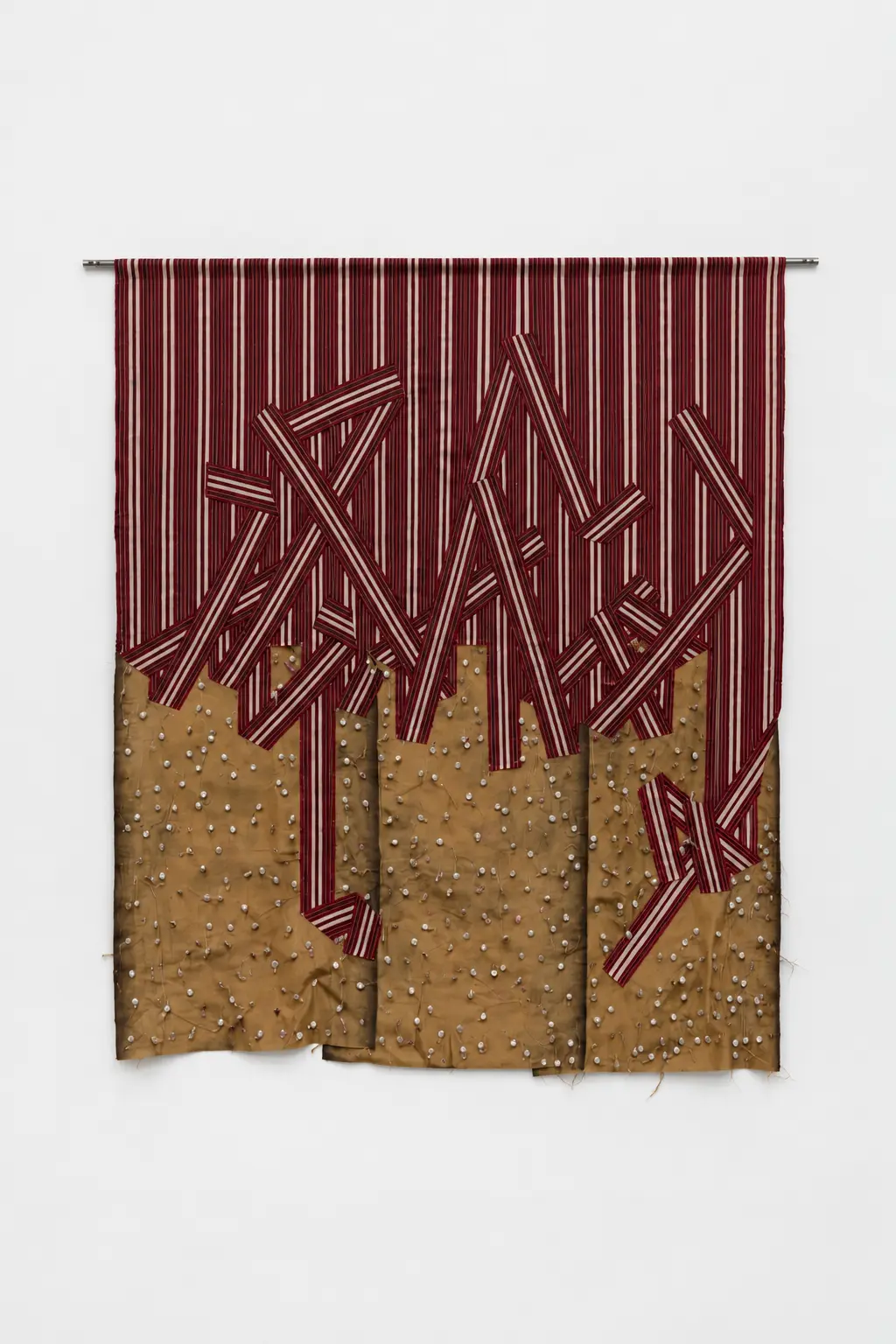 Ibrahim Mahama, Nyamuthia, 2025–2026. Hanging textile artwork combining burgundy and white striped fabric, overlapping geometric strips and brown cloth covered with small raised elements.