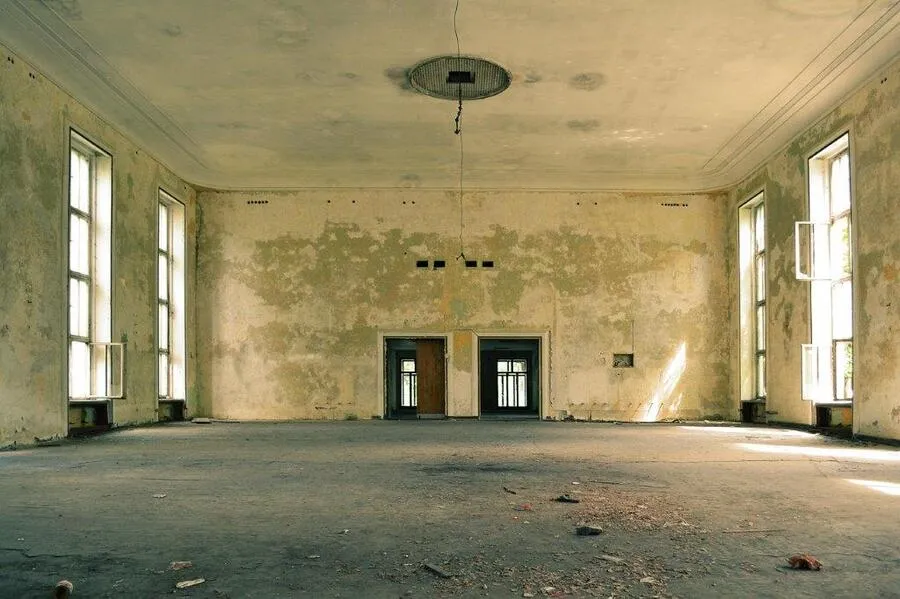 Empty hall with peeling plaster walls, tall windows and exposed concrete flooring in a historic building along the Naviglio Martesana.