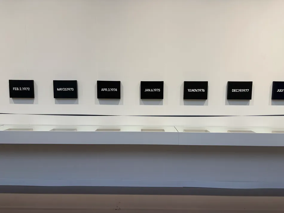 Series of small black rectangular paintings by On Kawara arranged horizontally on a white gallery wall, each displaying a date in white lettering.