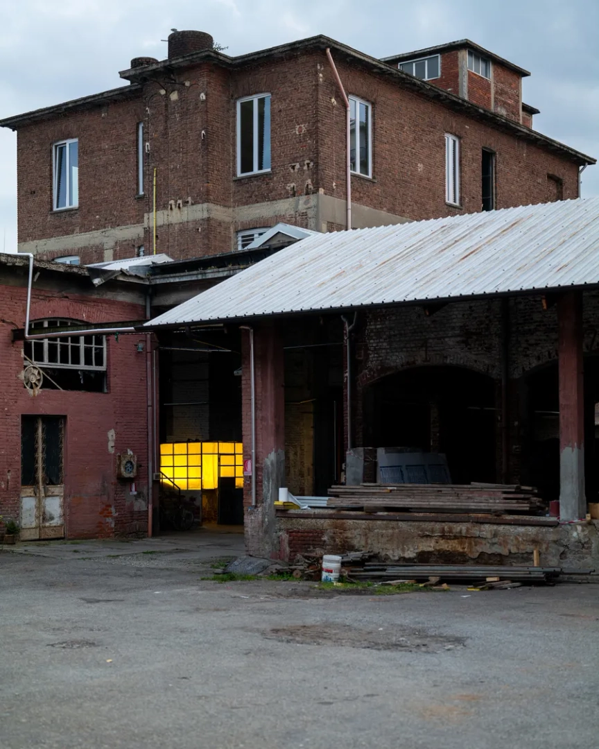 Paint It Black Torino exterior, a former industrial brick building with corrugated metal roofing, exposed structures and a yellow-lit entrance.