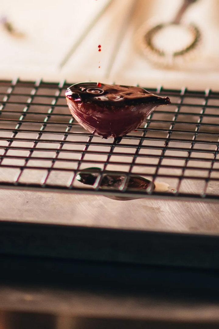 Dark sauce dripping onto a small culinary preparation resting on a metal rack in the kitchen.