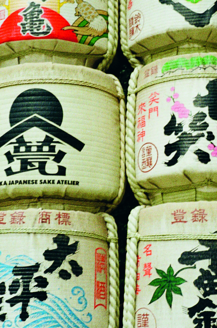 Traditional Japanese sake barrels wrapped in straw, decorated with black calligraphy, green mountain motifs, red seals and colorful floral emblems.