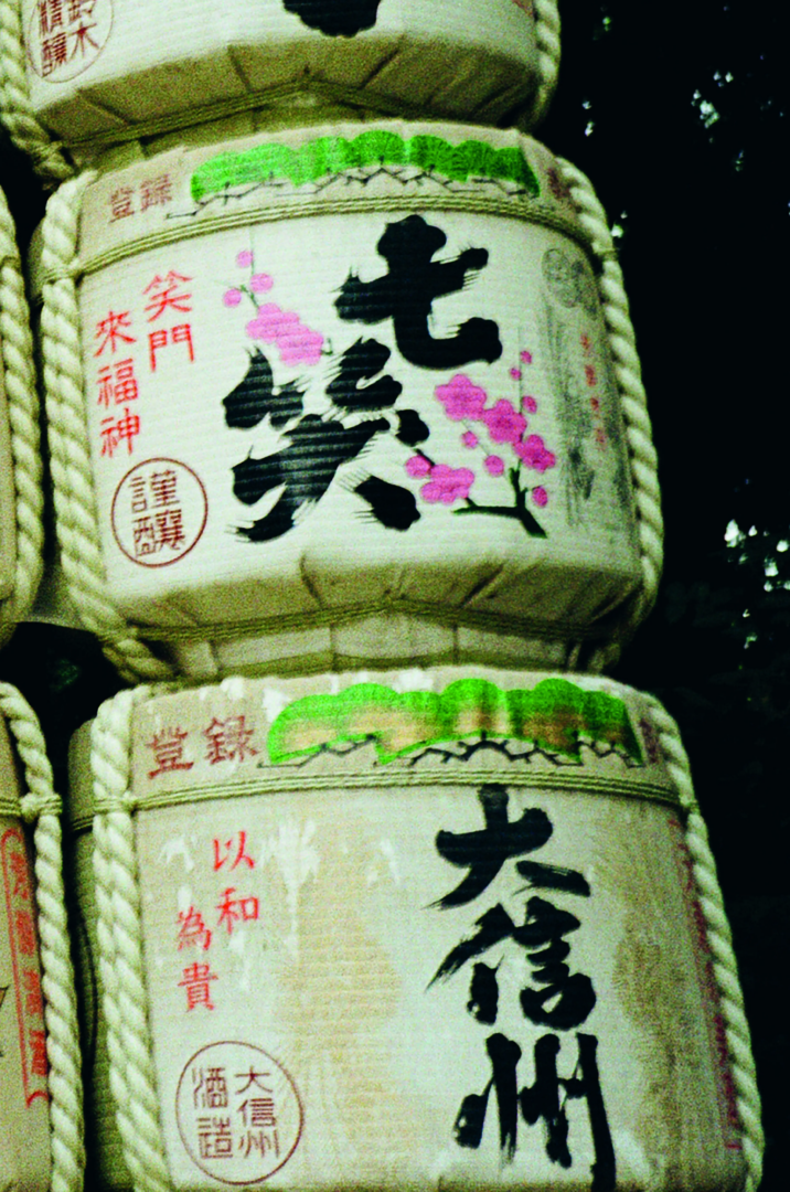 Traditional Japanese sake barrels wrapped in straw, decorated with black calligraphy, green mountain motifs, red seals and colorful floral emblems.