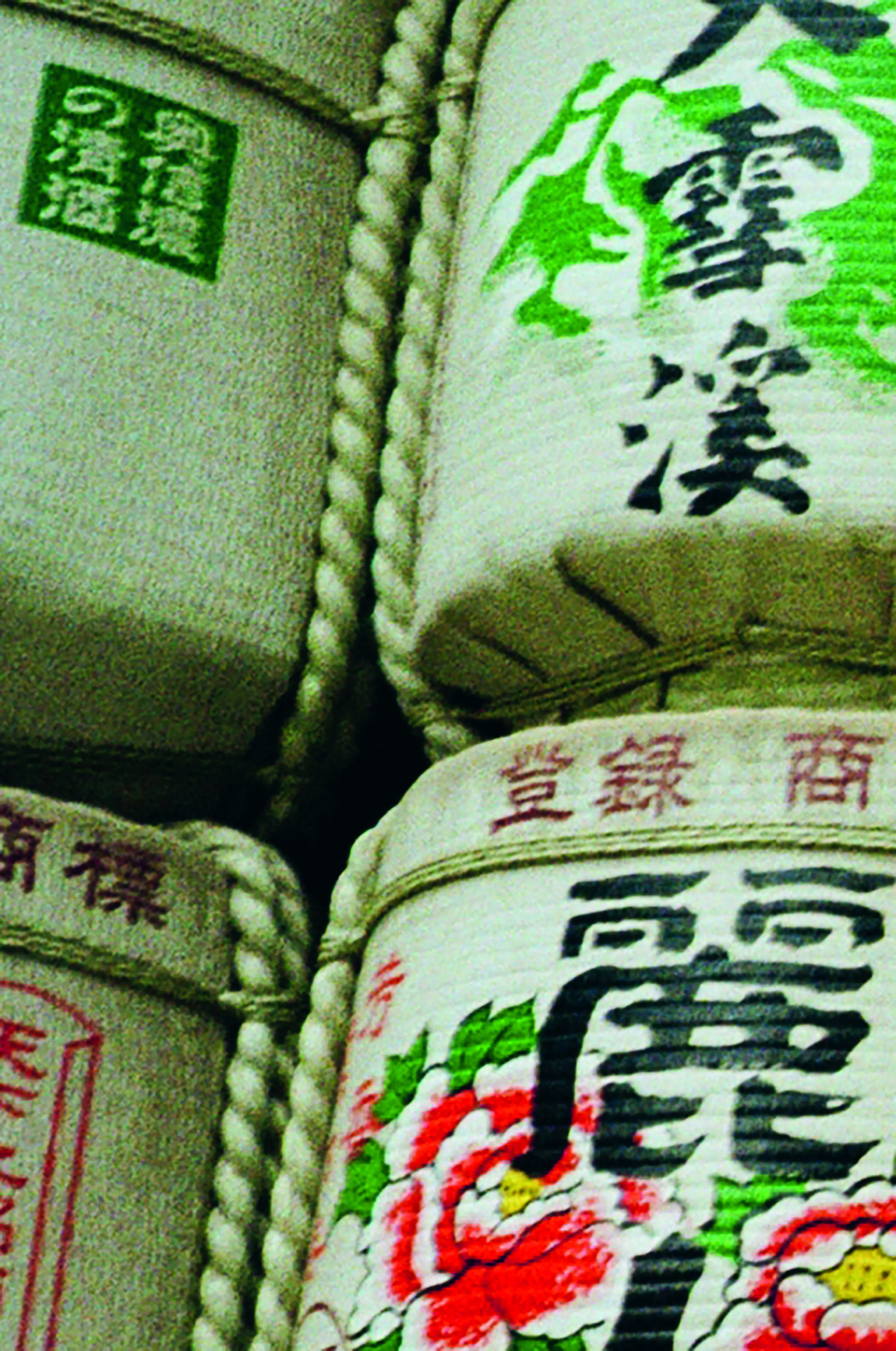 Traditional Japanese sake barrels wrapped in straw, decorated with black calligraphy, green mountain motifs, red seals and colorful floral emblems.