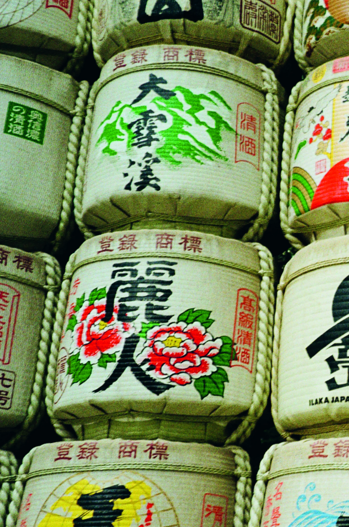 Traditional Japanese sake barrels wrapped in straw, decorated with black calligraphy, green mountain motifs, red seals and colorful floral emblems.