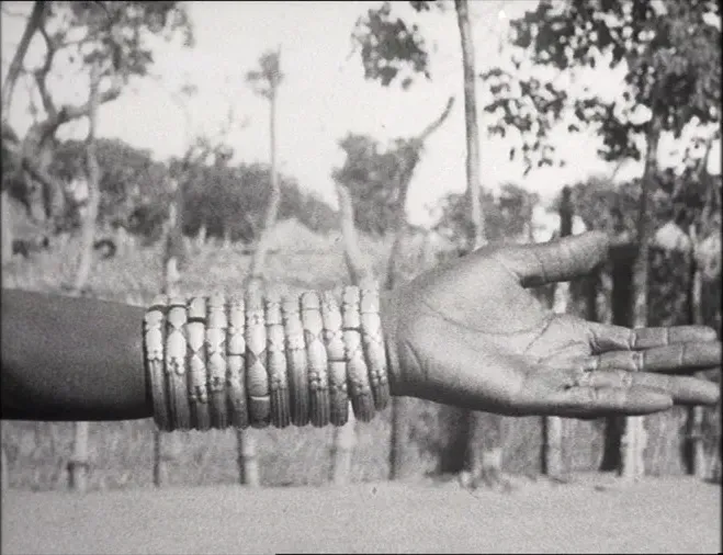 Black-and-white archival image from Sénégal en saison sèche (1920), showing an outstretched arm adorned with stacked bracelets against a landscape of trees.