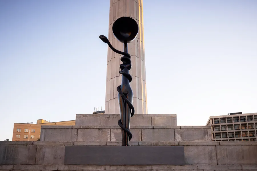 Simone Leigh's Sentinel (Mami Wata), a black sculptural figure entwined with a serpent, installed against a stone monument in New Orleans.