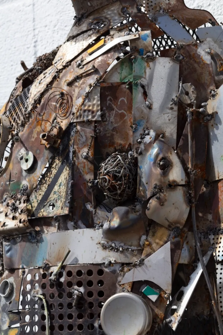 Close-up of a sculpture assembled from rusted metal sheets, welded fragments, perforated panels and coiled wire.